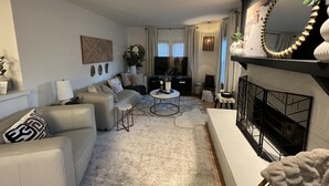 A modern living room with a sofa, coffee table, and fireplace. - Remodeled Riverside Cottage w/sunroom, She-shed. Walk to golf, tennis, Botanica, (Wichita)