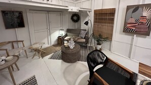 A cozy living room with a sofa, chairs, a coffee table, and a dining table. There is a wall with a framed picture and a hanging light fixture. - Remodeled Riverside Cottage w/sunroom, She-shed. Walk to golf, tennis, Botanica, (Wichita)