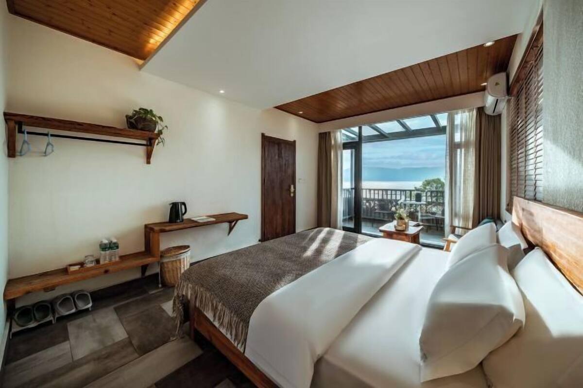 A bedroom with a large bed, wooden beams, a balcony, and a view.