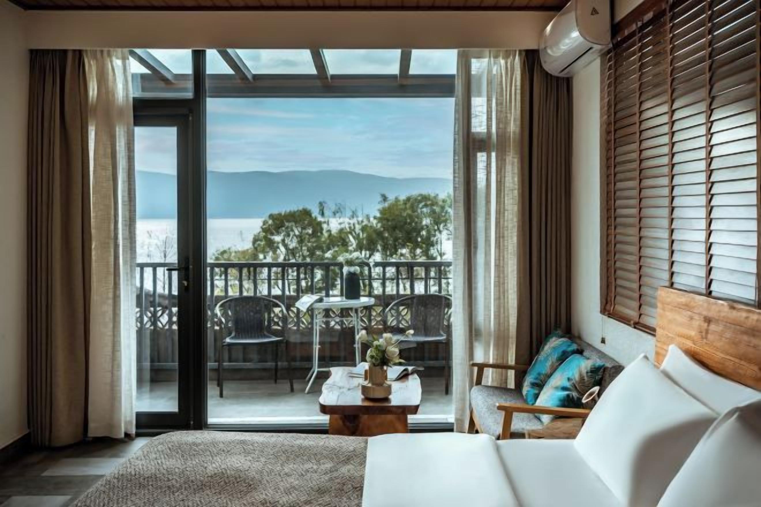 A room with a bed, a sofa, a coffee table with flowers, and a view of a balcony with chairs and a table.