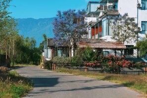 Una carretera que lleva a un edificio tradicional con techo de paja y montañas al fondo.