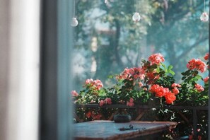 A window with a view of a wooden table and a potted plant with red flowers. - Perch House (Dali City)