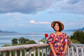 A person standing on a balcony with a railing, overlooking a body of water and distant mountains. - Perch House (Dali City)