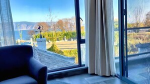 A room with a large window, a chair, and a view of a landscape with trees and a body of water. - Perch House (Dali City)
