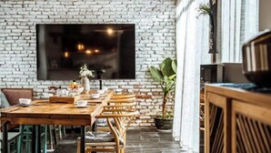 A dining area with a brick wall, a large flat-screen TV mounted above a wooden table and chairs, and a potted plant to the side. - Perch House (Dali City)
