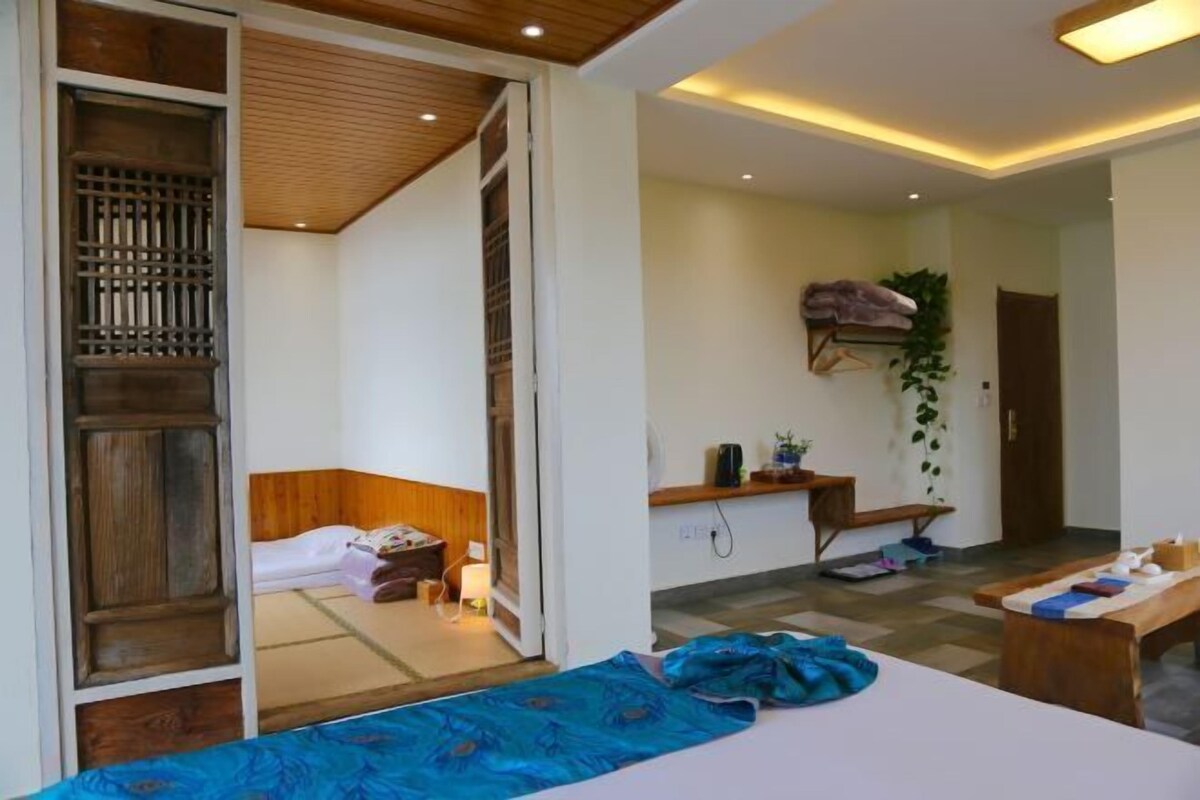 A room with a bed, a desk, and a small table. There is a sliding door leading to another room.