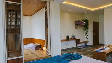 A room with a bed, a desk, and a small table. There is a sliding door leading to another room.