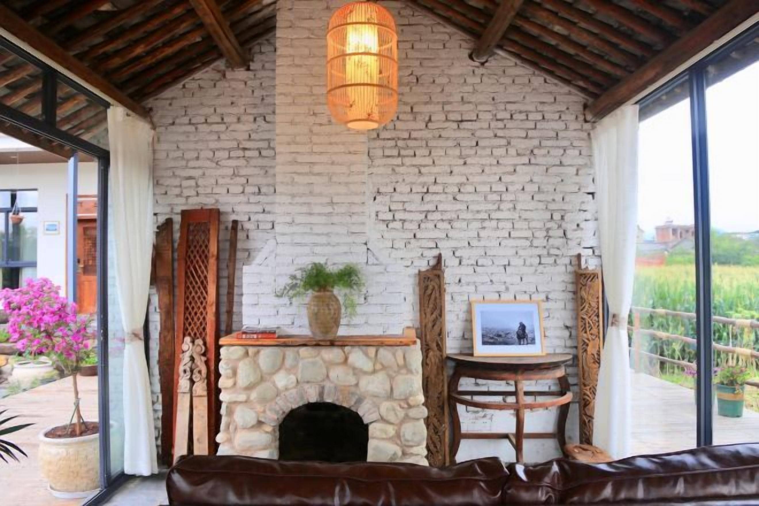 Una habitación con chimenea de piedra, sofá de cuero y un amplio ventanal con vistas a un jardín.