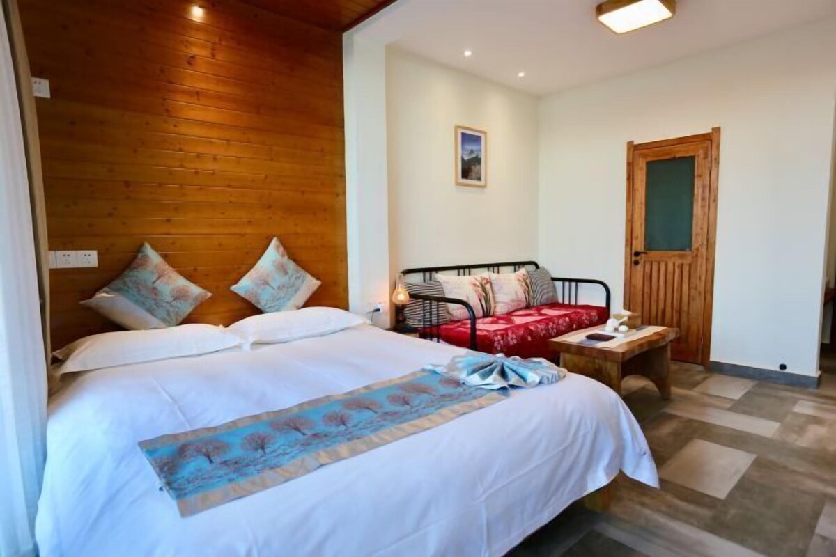 A bedroom with a wooden headboard, a bed with white bedding and a blue decorative runner, a bedside table with a lamp, and a wooden door.
