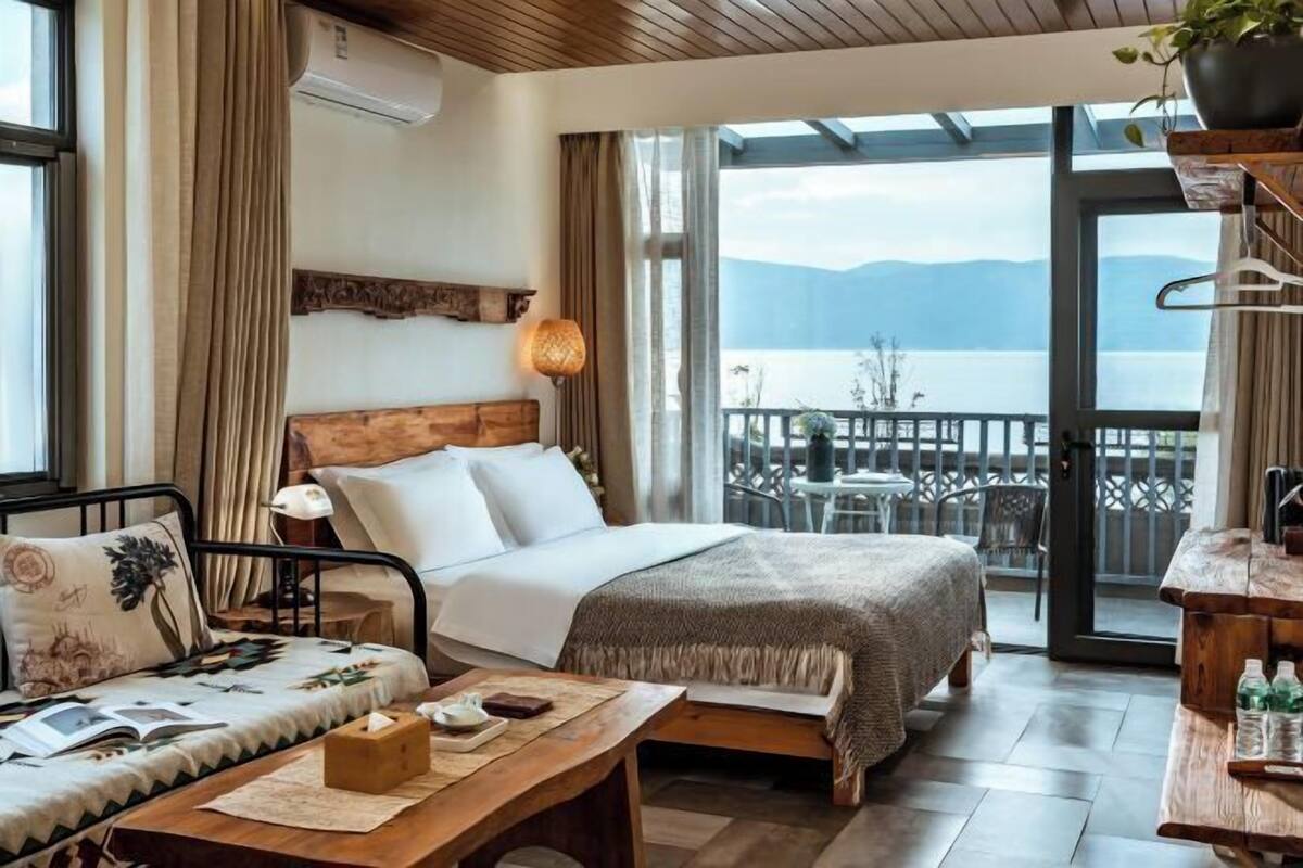 A bedroom with a bed, bedside table, and a view of a balcony with outdoor furniture.