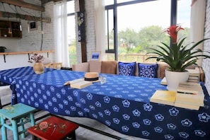 A room with a table covered by a blue tablecloth, a potted plant, and a window with a view of greenery. - Perch House (Dali City)