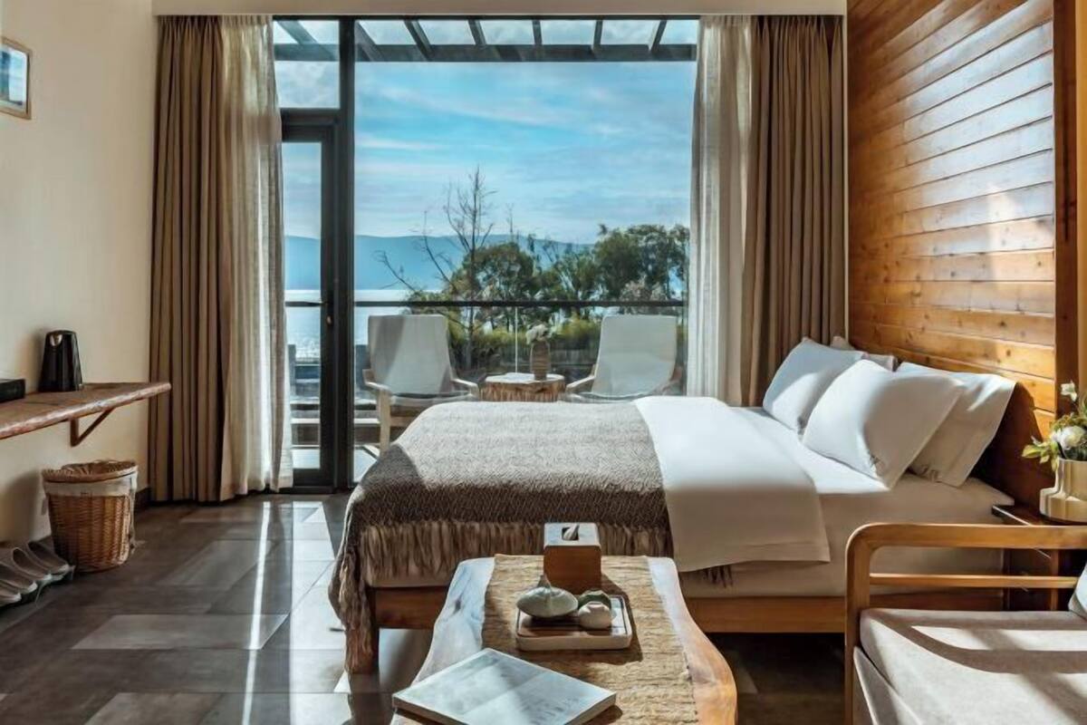 A hotel room with a bed, a desk, a chair, a small table with a tray, and a view of the outdoors.