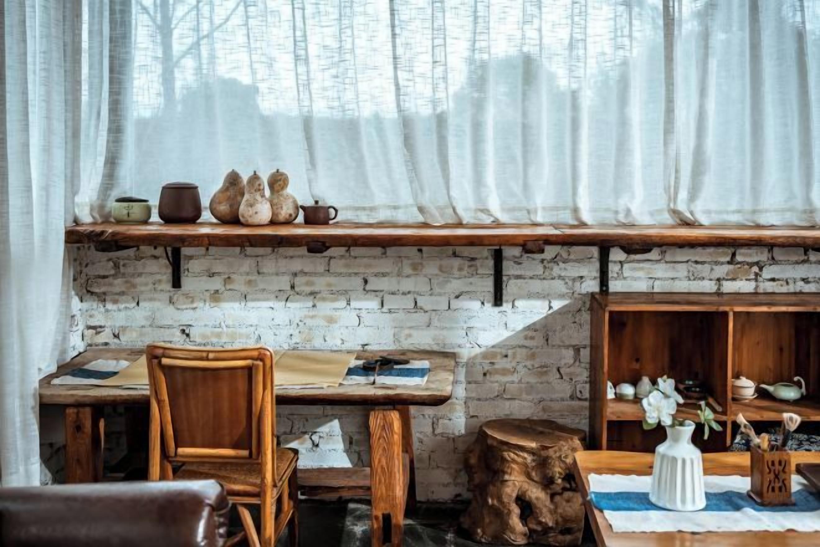 Un interior rústico con pared de ladrillo, muebles de madera y una estantería con cerámica.