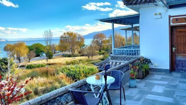 A terrace with a table and chairs, overlooking a body of water and trees. - Perch House (Dali City)