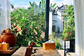Un jardin chinois traditionnel avec une table en bois, un pot en argile et une vue sur un élément d’eau et une architecture traditionnelle.