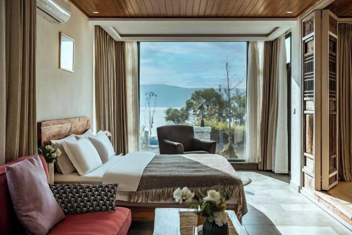 A bedroom with a bed, a chair, a red sofa, and a view of the outdoors.
