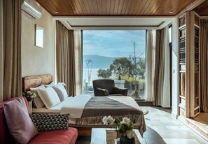 Ein Schlafzimmer mit Bett, Sessel, rotem Sofa und Blick ins Freie.