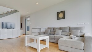 Una sala de estar moderna con un sofá gris, una mesa de centro blanca y un televisor sobre un mueble blanco.