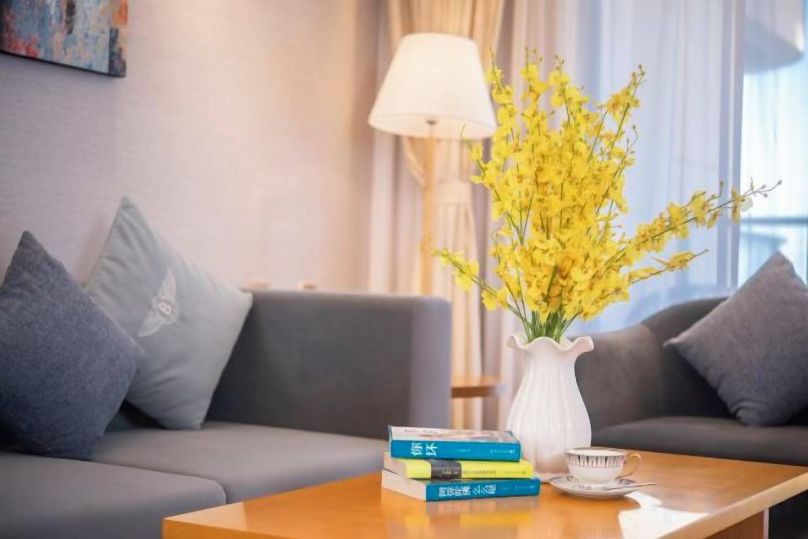 A living room with a sofa, a coffee table with books and a vase of flowers, and a lamp.