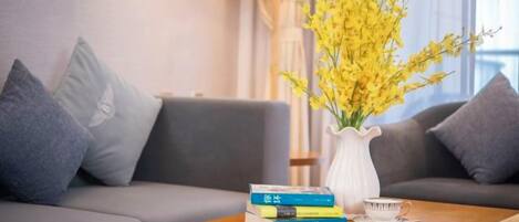 A living room with a sofa, a coffee table with books and a vase of flowers, and a lamp.
