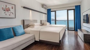 Habitación de hotel moderna con una cama grande, un sofá, un televisor y un balcón con vistas al mar.