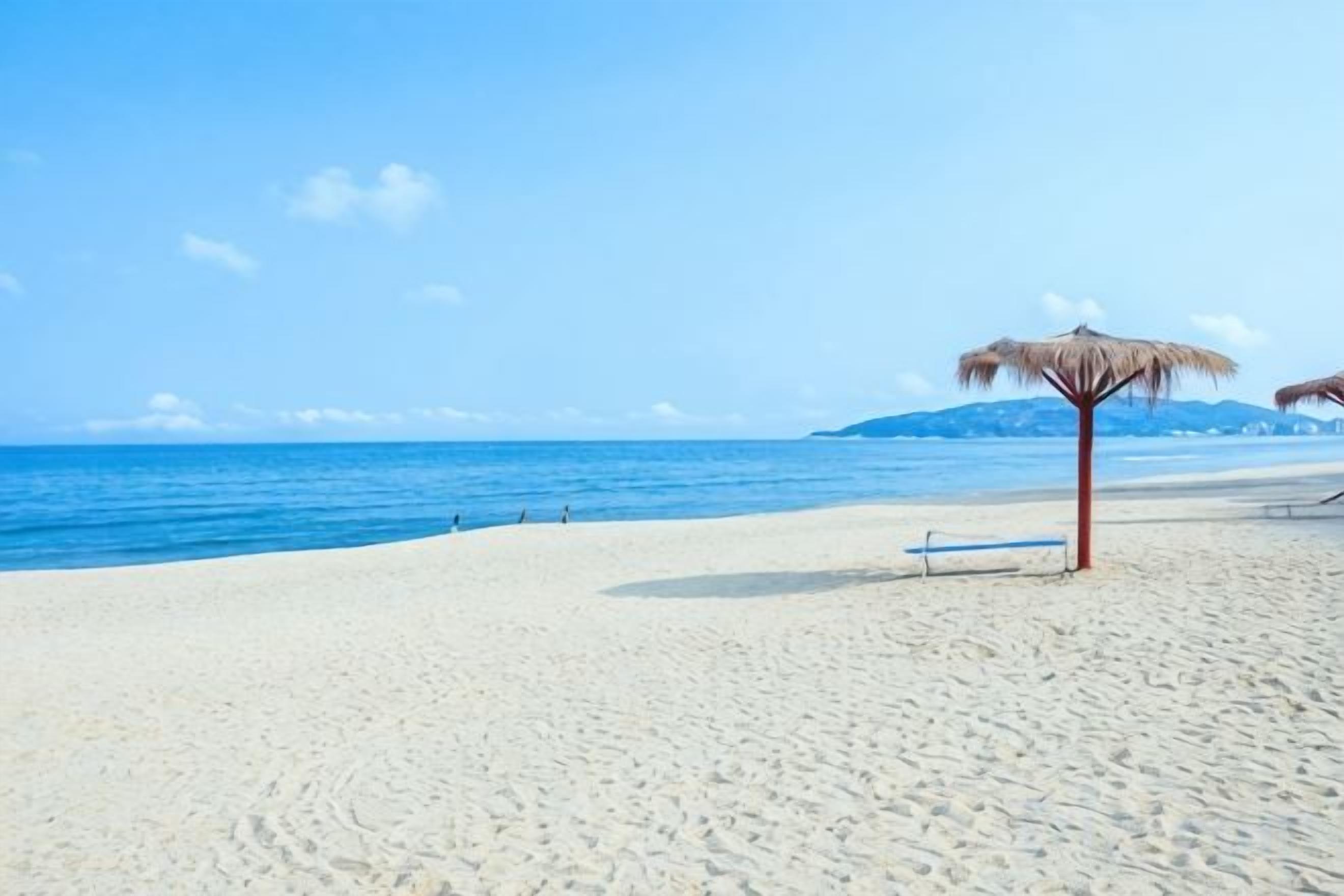 A beach with a clear sky, a sandy shore, and a thatched umbrella.