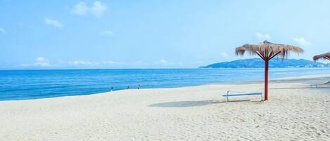 A beach with a clear sky, a sandy shore, and a thatched umbrella.