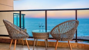Un balcón con sillas de mimbre y una mesa de vidrio, con vista al mar.