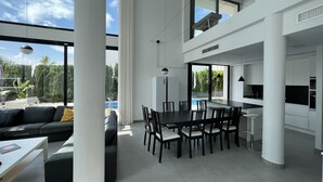 Un intérieur spacieux et moderne comprenant une grande salle à manger, une cuisine et un salon avec vue sur une piscine et un espace verdoyant.