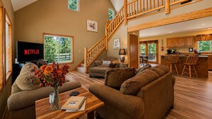 A spacious living area with a high ceiling, a wooden staircase, a kitchen with wooden cabinets, and a dining area. - Views | Dogs | Hot Tub | Firepit | BBQ | Family (Leavenworth)
