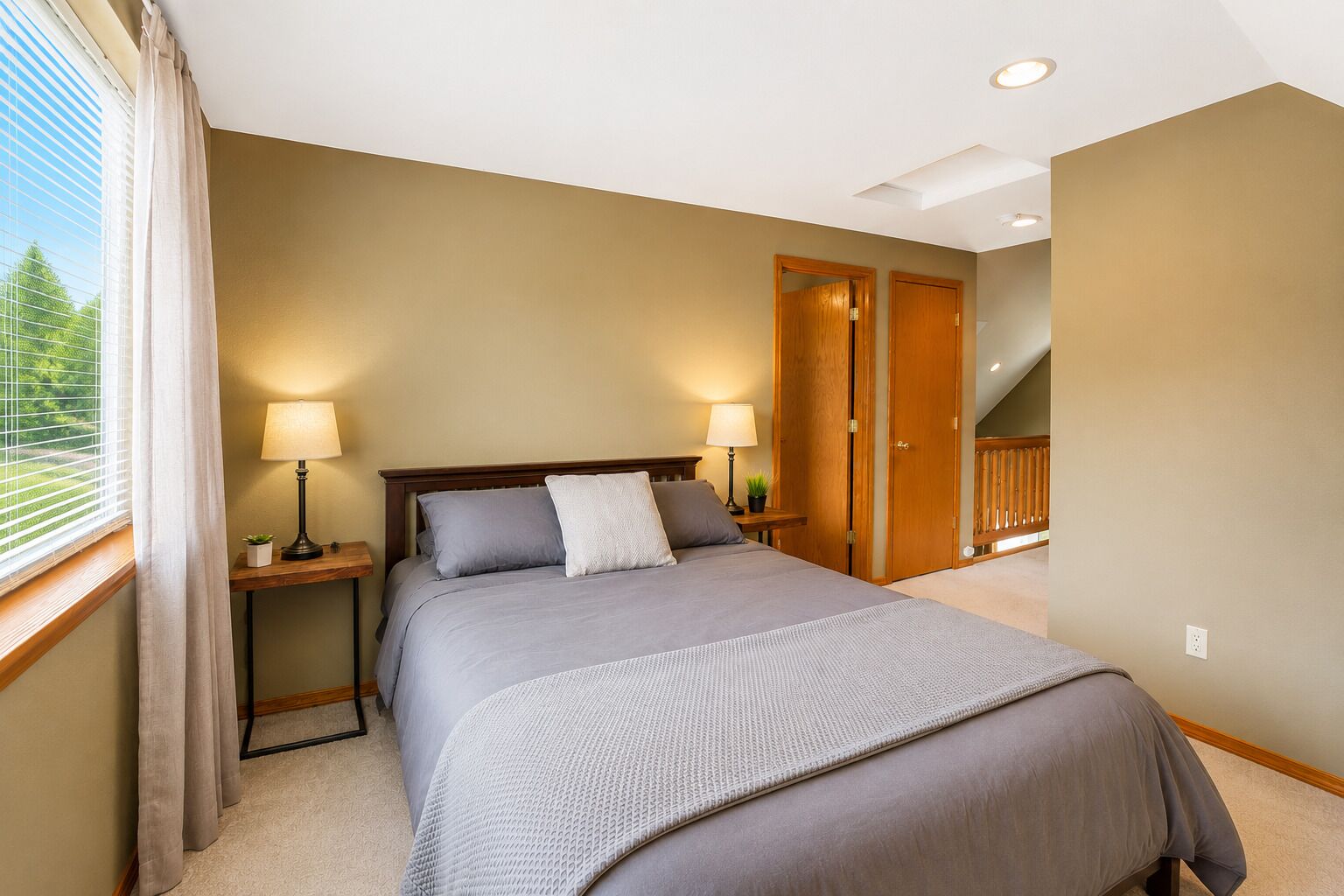 A bedroom with a bed, two bedside tables, a lamp, a potted plant, and a view of a balcony.
