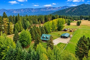 Ein ländliches Anwesen mit mehreren Gebäuden, darunter ein Haupthaus und verschiedene Nebengebäude, umgeben von dichtem Wald und Bergen im Hintergrund.