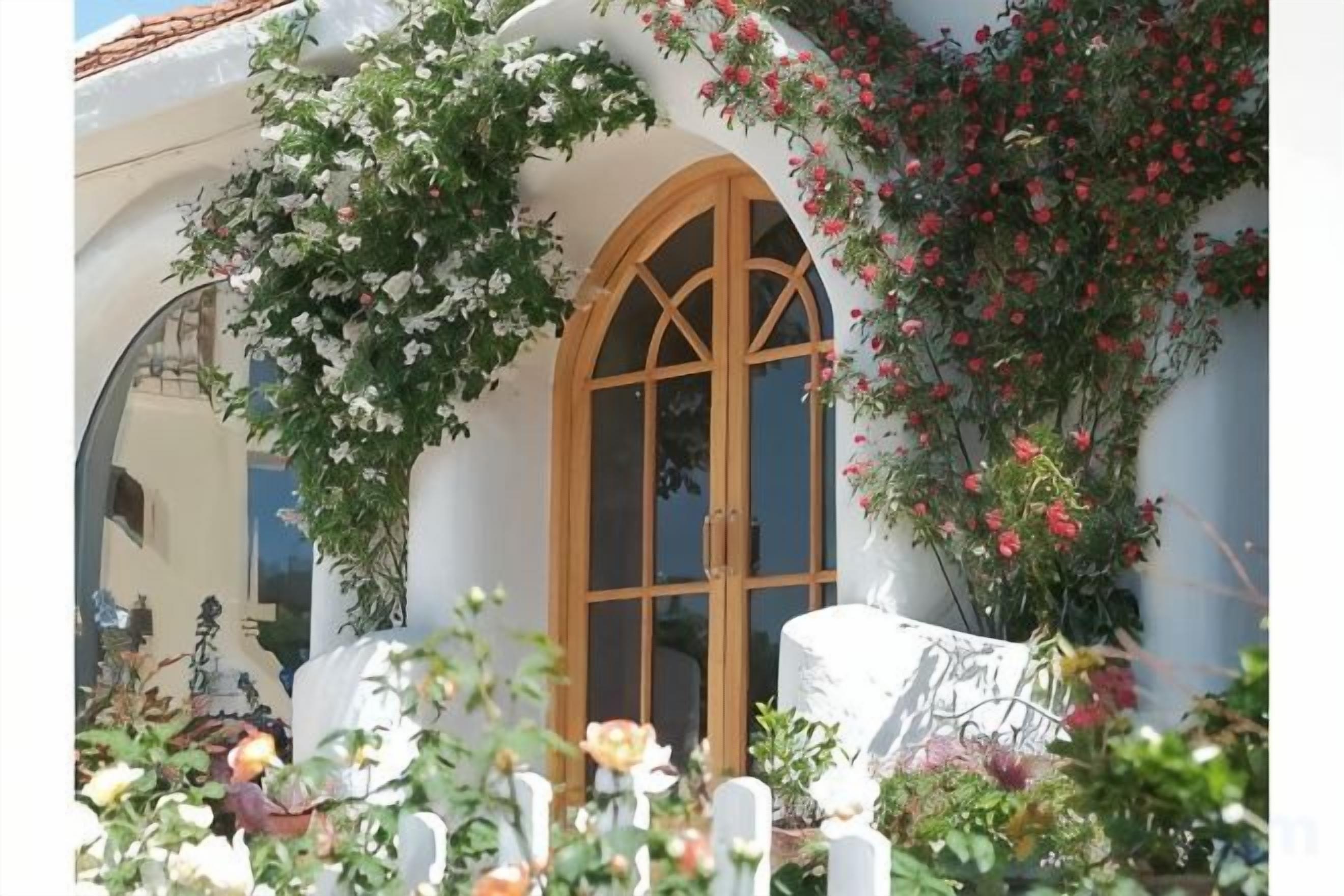 Un edificio con un amplio arco de entrada, rodeado de exuberante follaje y plantas florecientes.