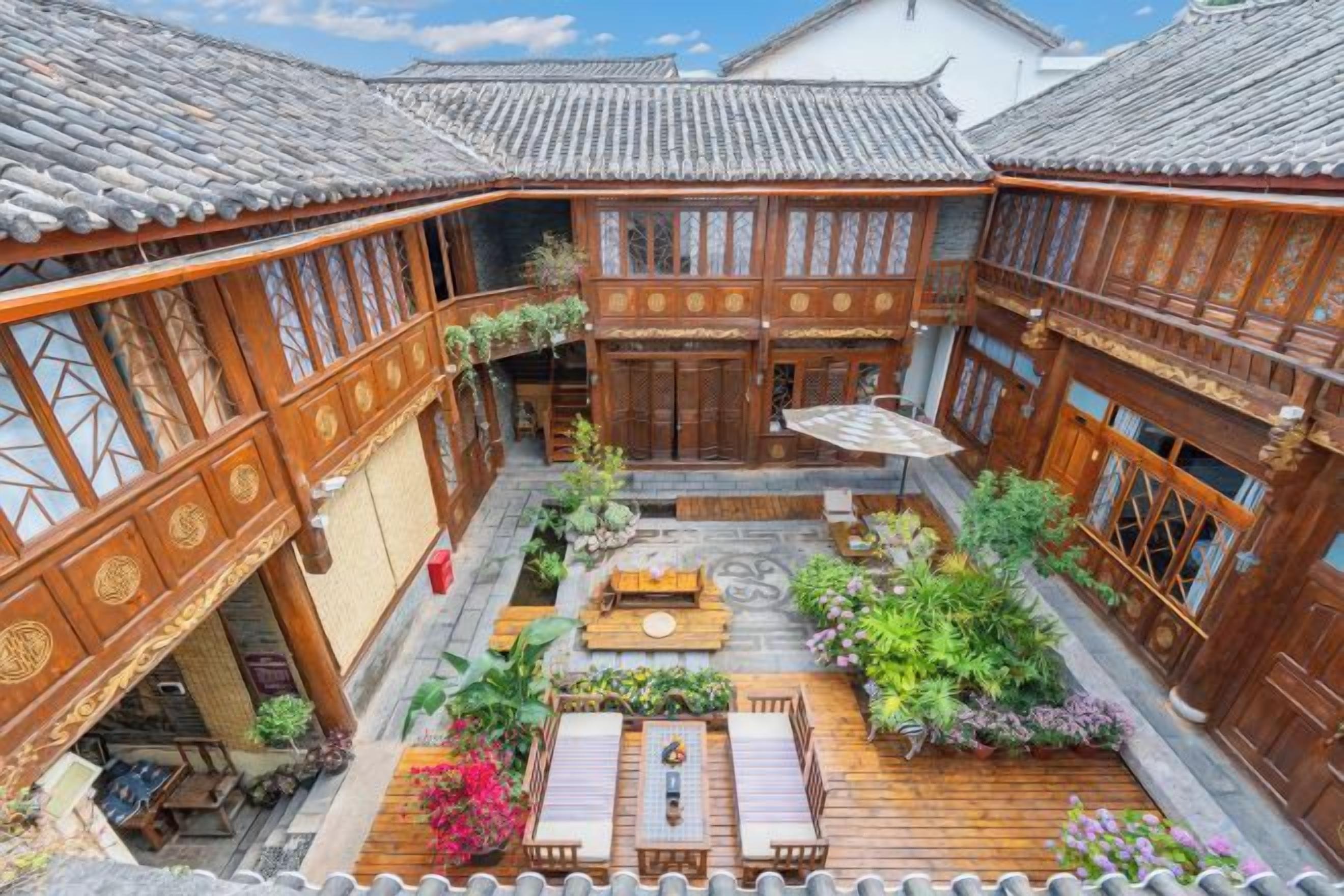 A courtyard with wooden buildings, a central seating area, and potted plants.