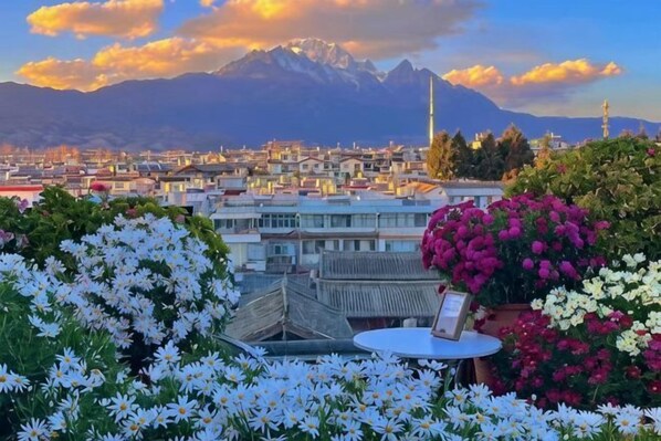 A cityscape with mountains in the background, a table with flowers, and a clear sky.