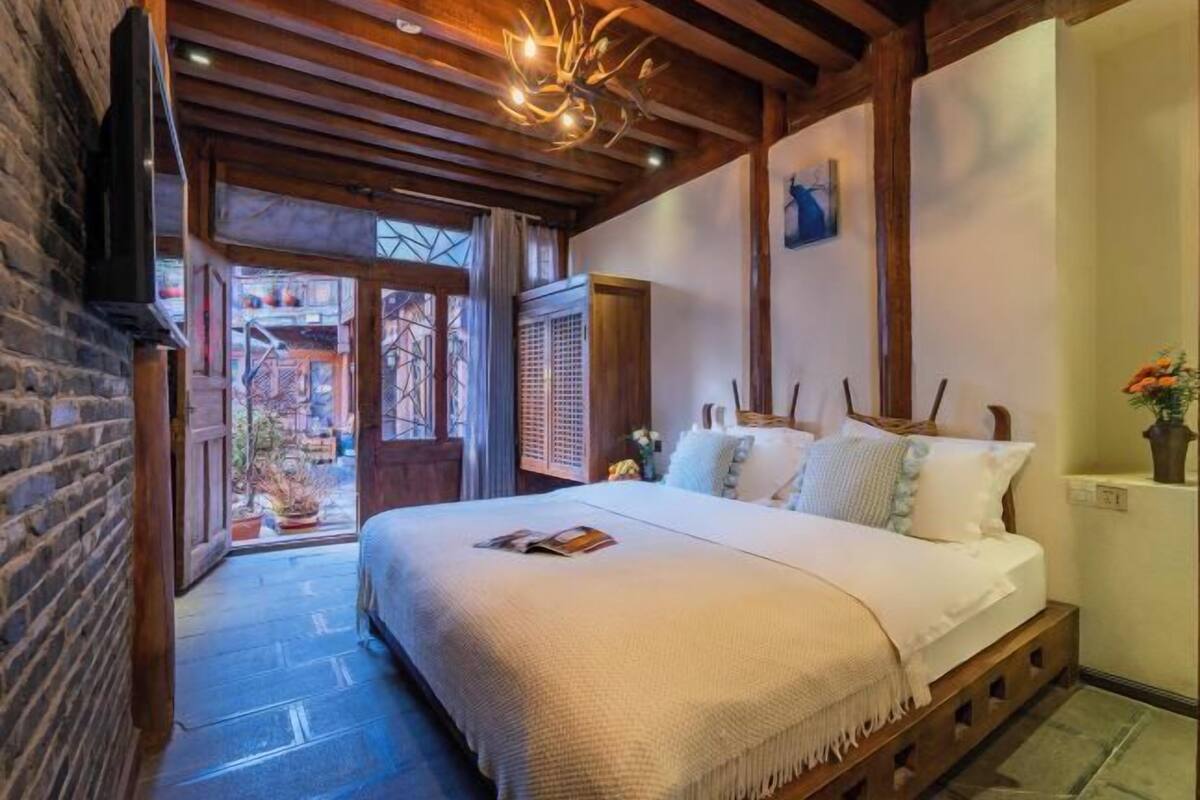 A bedroom with a bed, wooden beams, a TV, and a view of the outside.