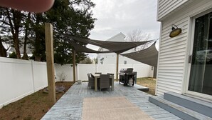 A wooden deck with a table and chairs, a grill, and a shaded area. - Bayside Retreat: Your Perfect Beach Getaway (Lower Township)