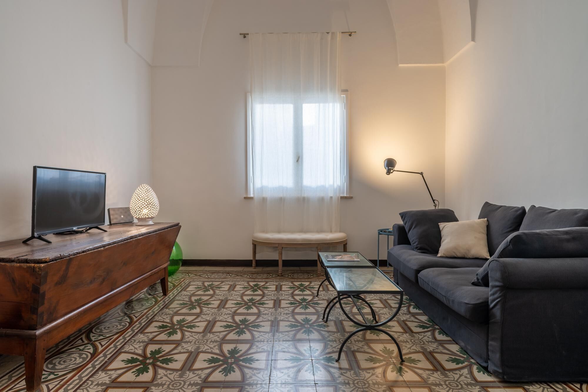 Un salon avec un téléviseur, une lampe, un canapé et un sol à motifs.