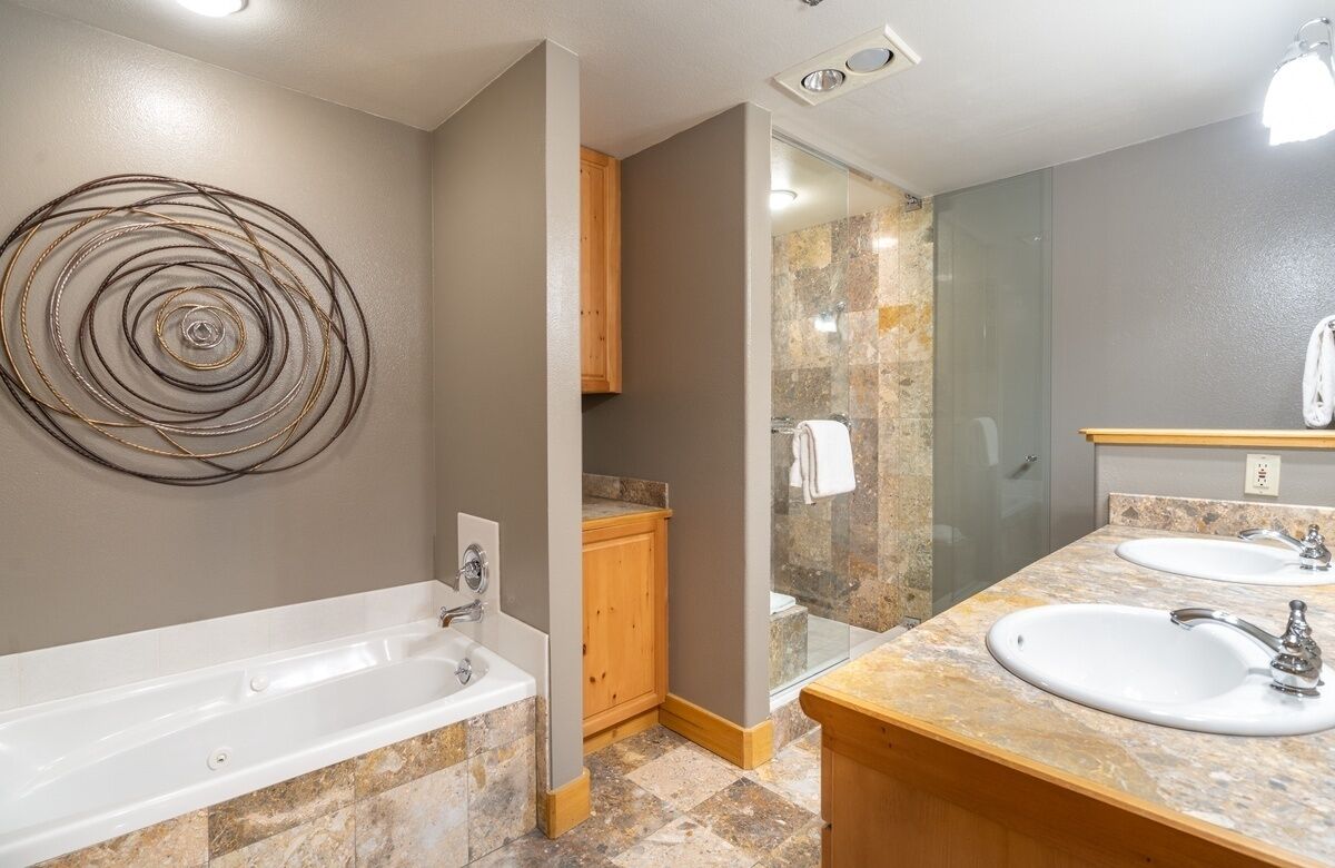 A modern bathroom with a bathtub, two sinks, a glass shower enclosure, and a wooden cabinet.