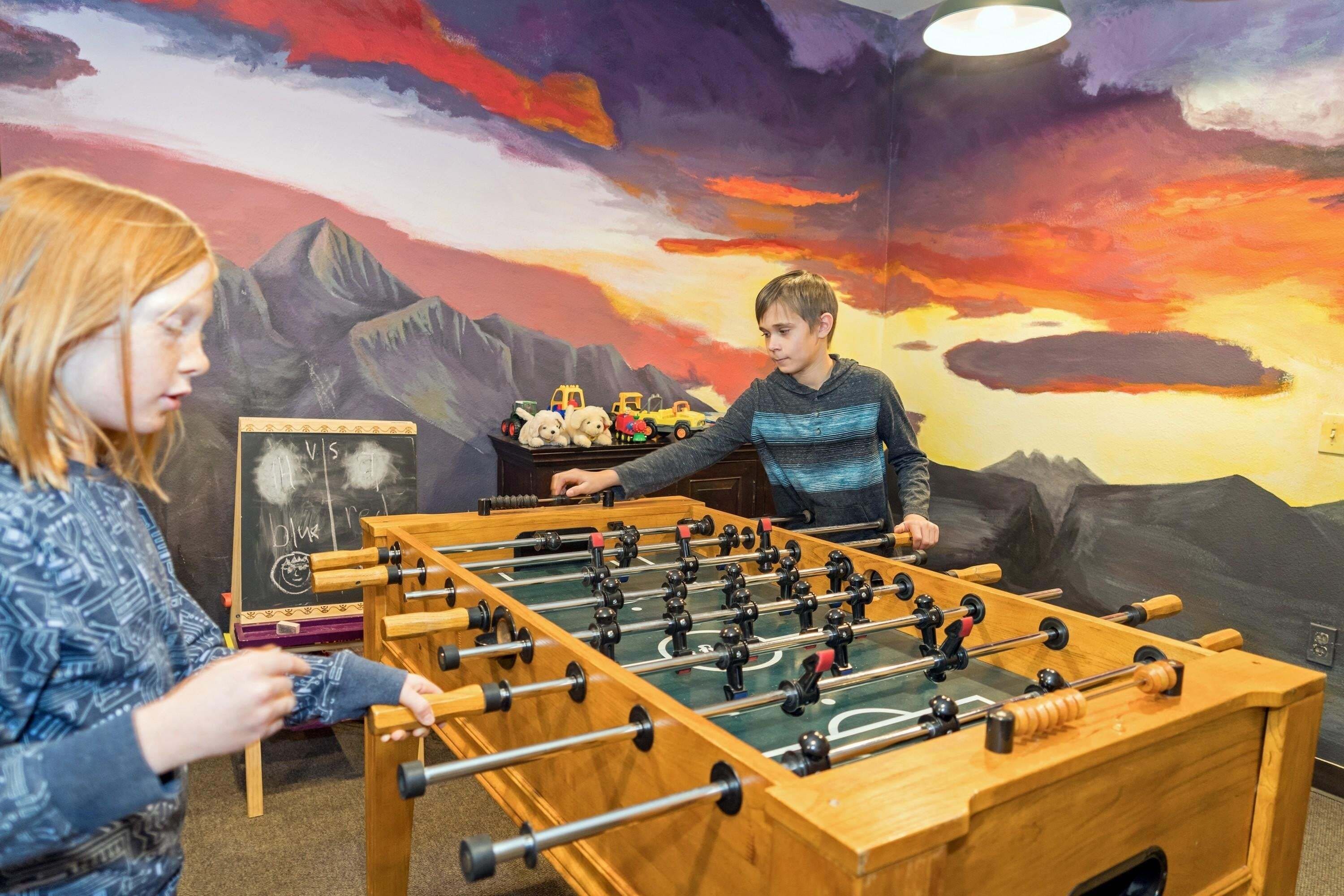A foosball table in a room with a mural of a sunset over mountains.