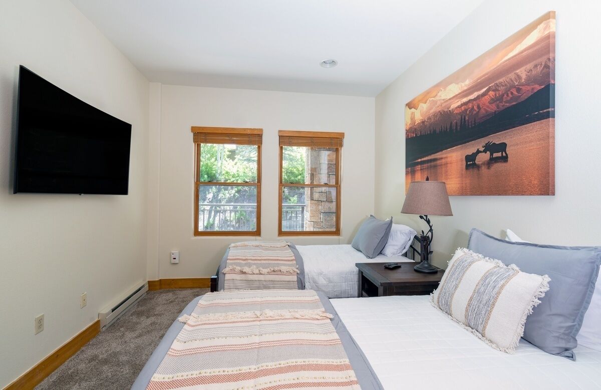 Hotelkamer met twee bedden, een flatscreen televisie, een schilderij van een eland en een raam met uitzicht op bomen.