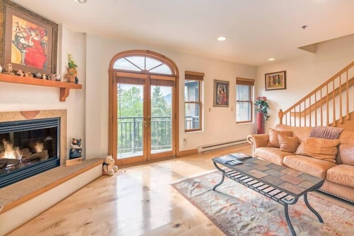 A spacious living room with a fireplace, a leather sofa, a coffee table, and a staircase.