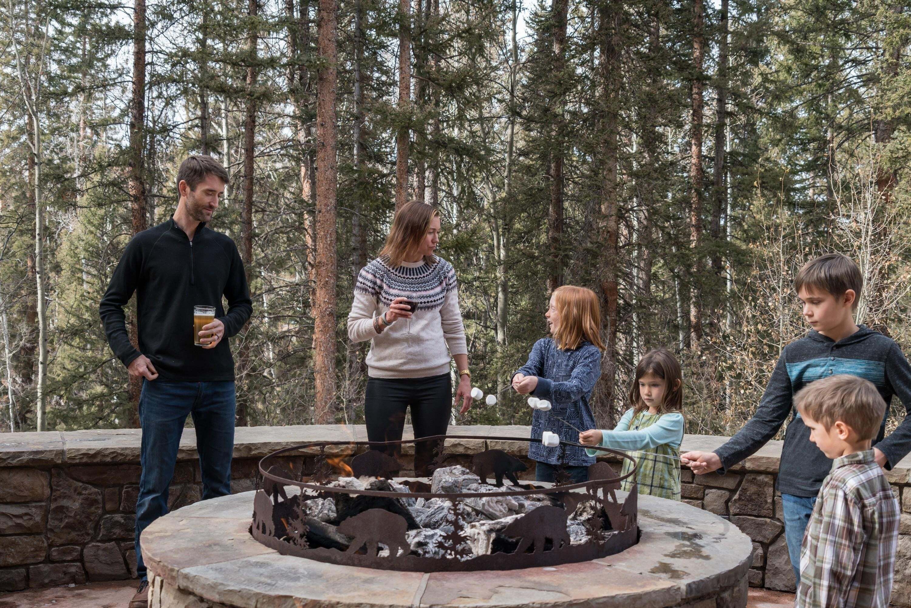 A group of people around a stone fire pit with animal silhouettes, set in a forested area.