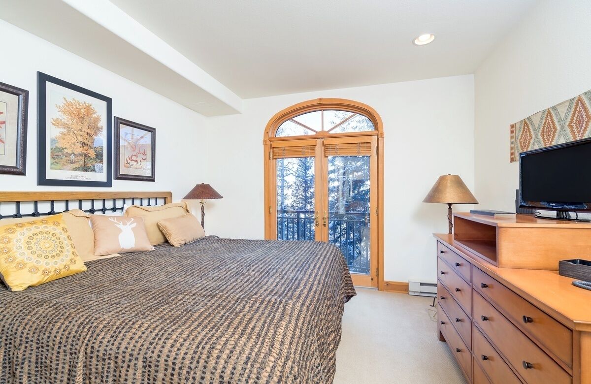 A bedroom with a bed, a dresser, a television, and a window with a view of trees.