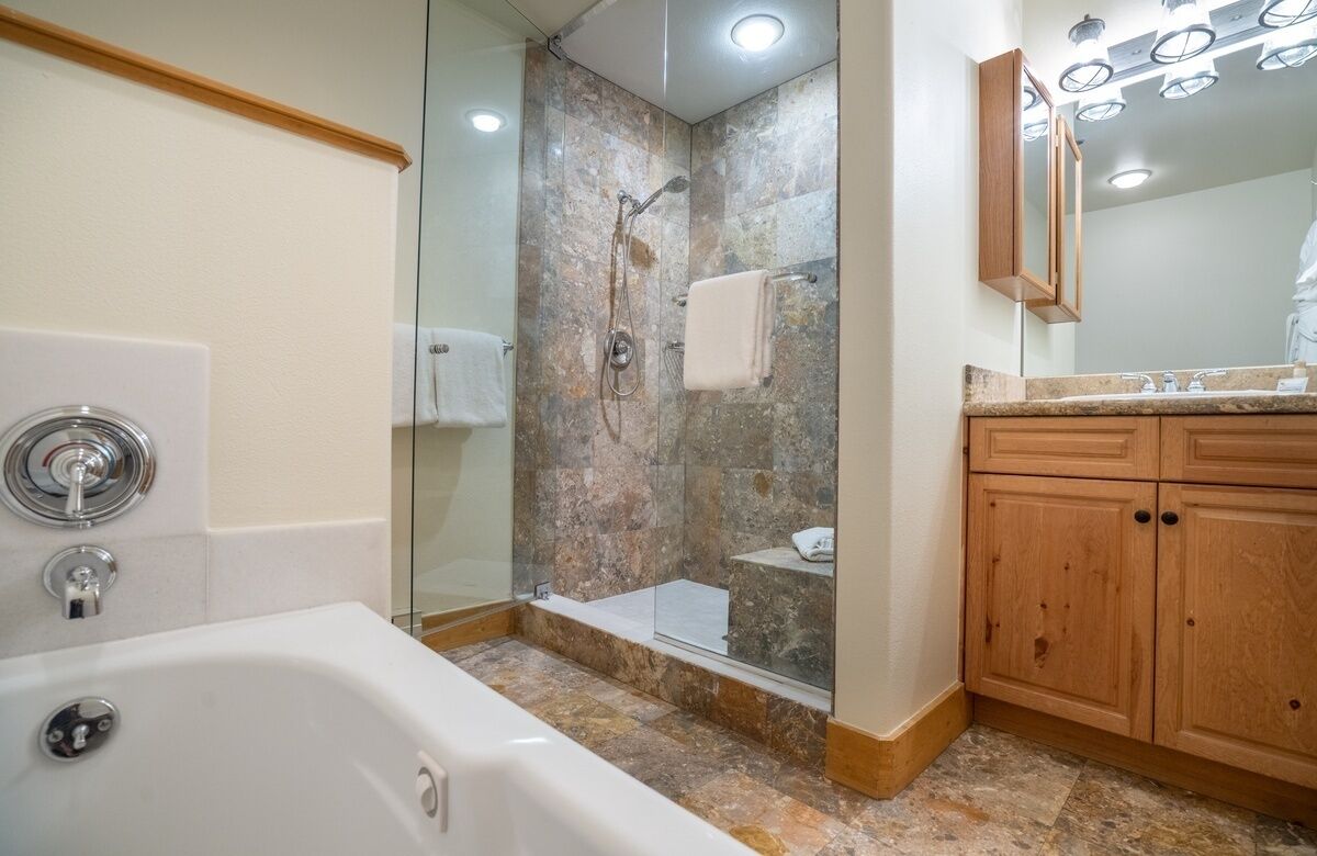 Un baño con bañera, ducha envuelta en vidrio y armarios de madera.