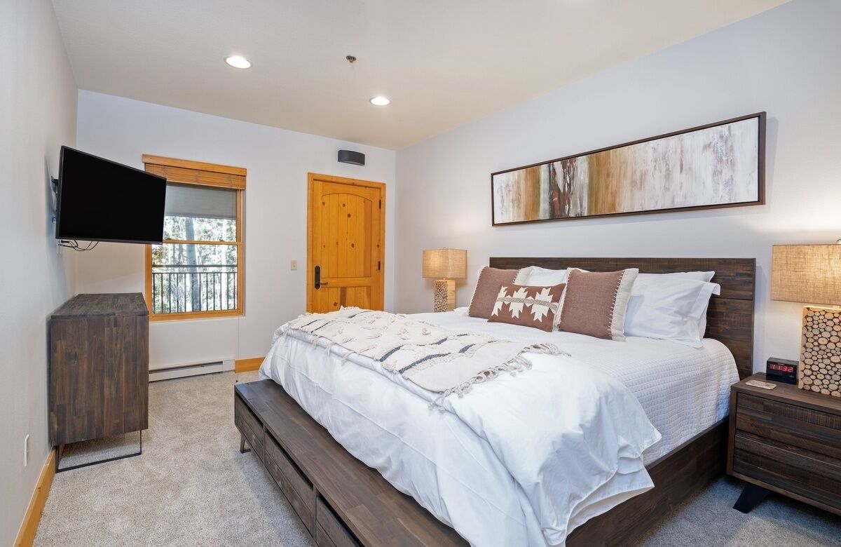 A bedroom with a bed, bedside tables, a TV, a wooden door, and a window.
