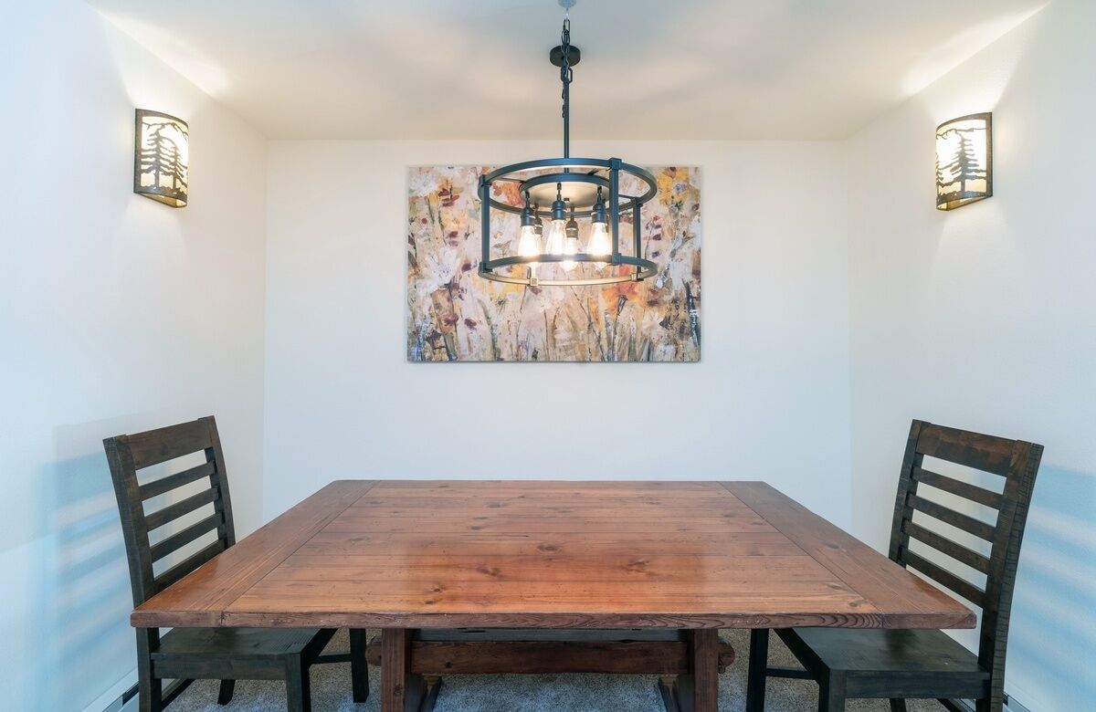Un comedor con una mesa y sillas de madera, una araña y lámparas fijadas a la pared.