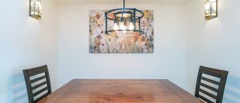 Un comedor con una mesa y sillas de madera, una araña y lámparas fijadas a la pared.