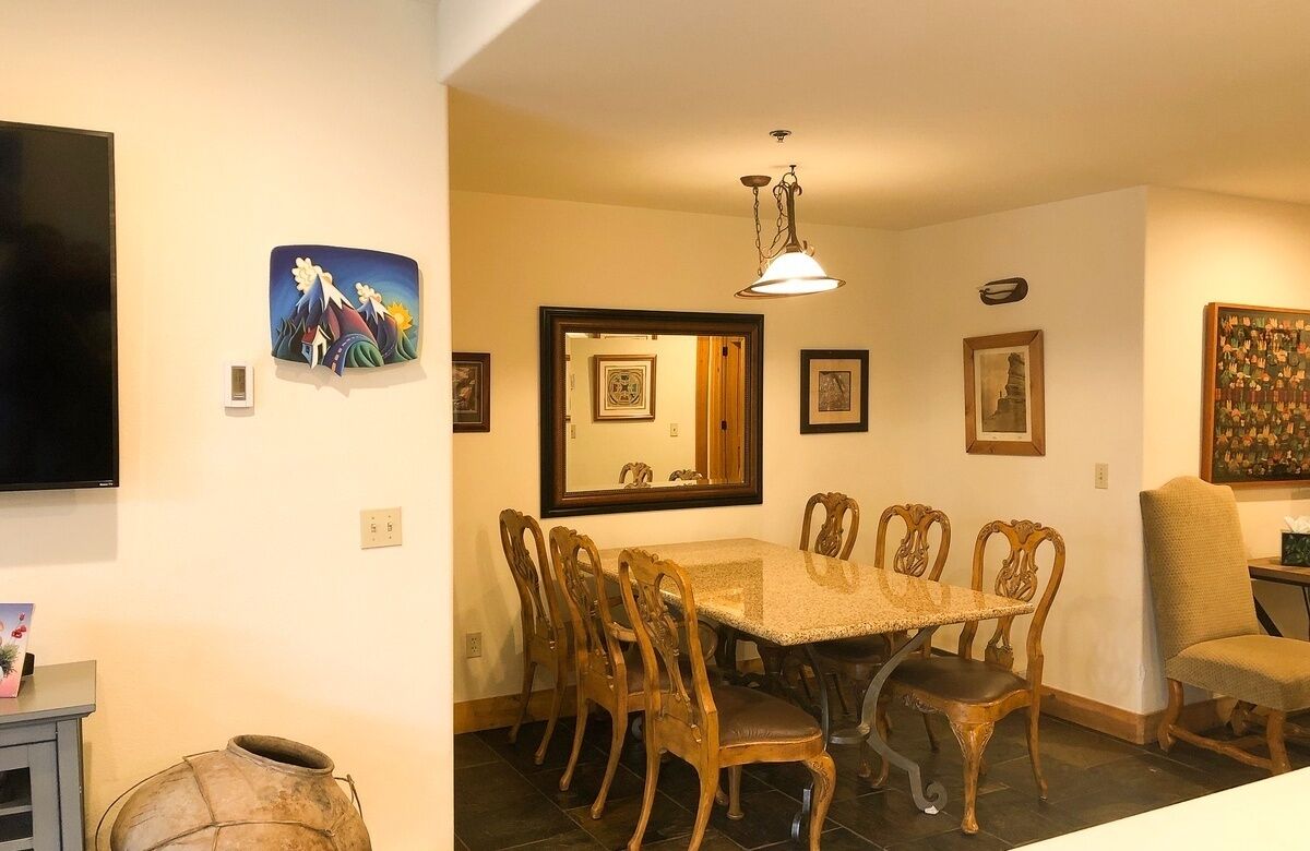 A dining area with a rectangular table, six wooden chairs, a chandelier, and various framed artworks on the walls.