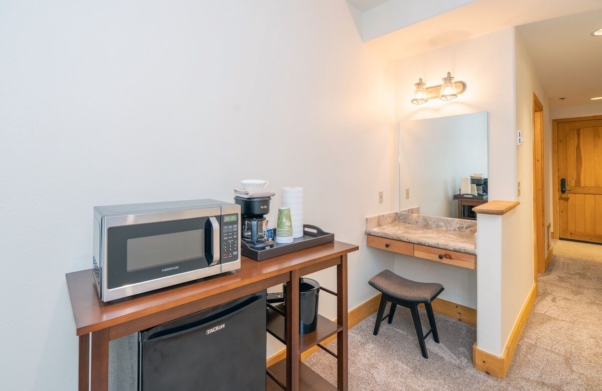 Una kitchenette compacta con microondas, cafetera y refrigerador pequeño.
